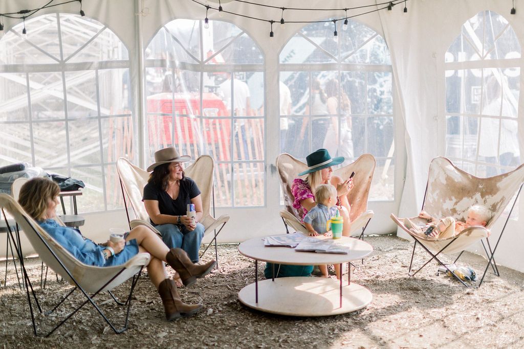 People relaxing in hanging chairs inside a clear tent with string lights and a low round table