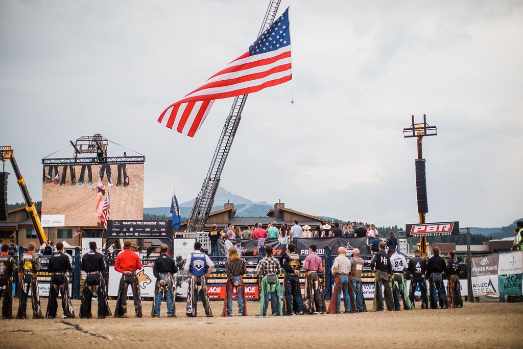 Crowd watching a flag display and cranes at an outdoor event under a cloudy sky