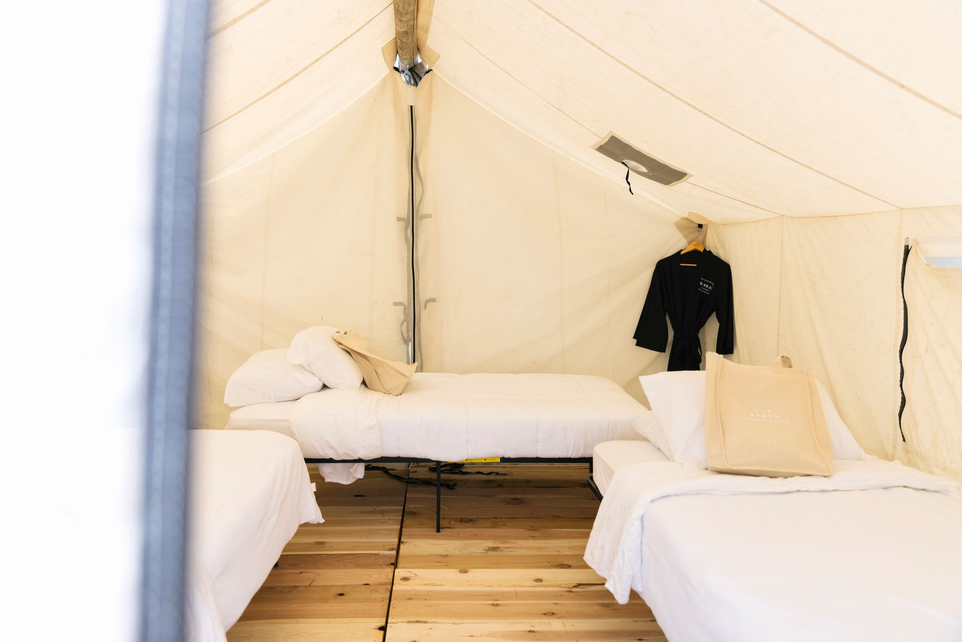 White tent interior with three beds, wooden floor, and a black jacket hanging on the wall