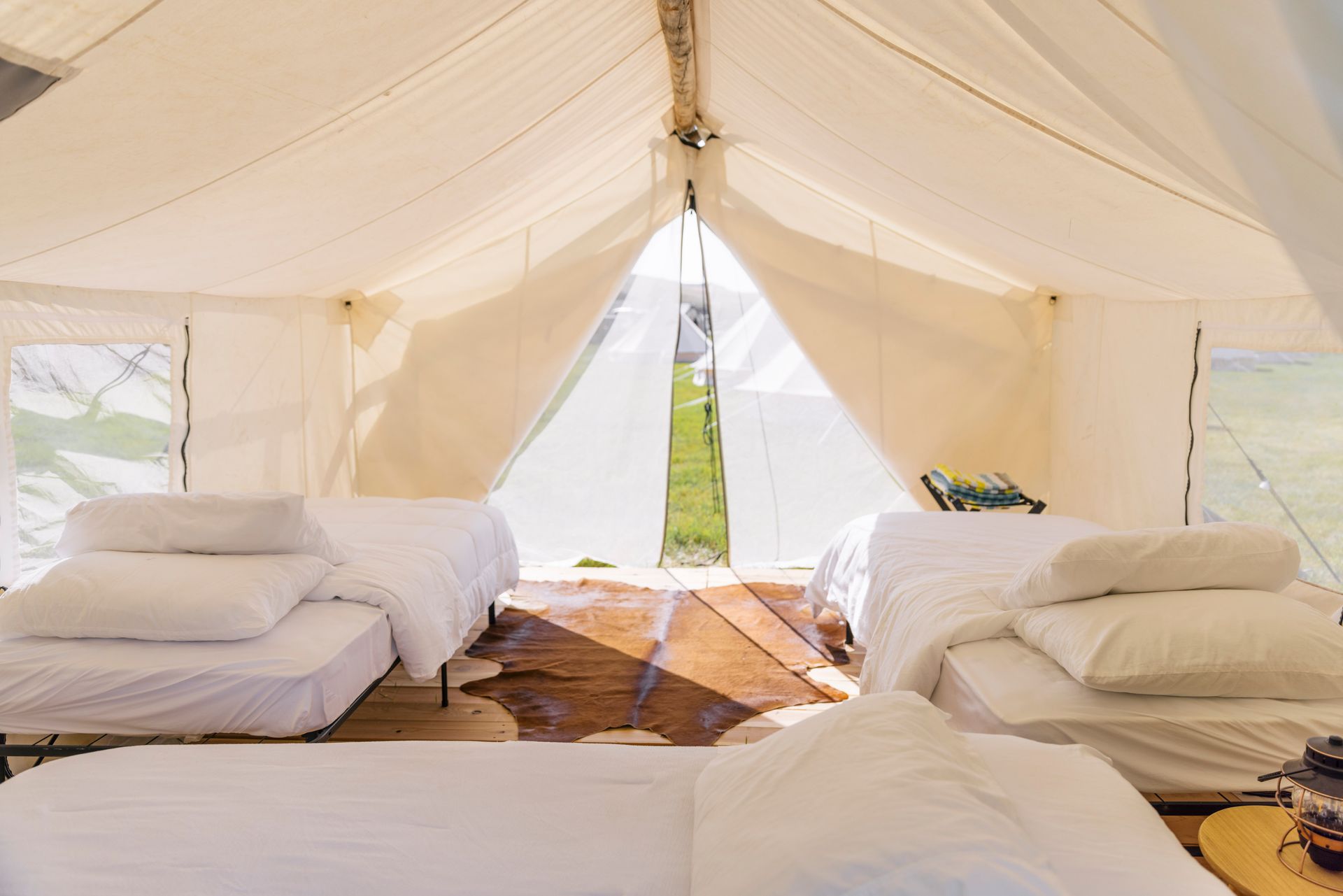 Interior of a white canvas tent with beds and pillows on both sides and sunlight streaming through the center opening