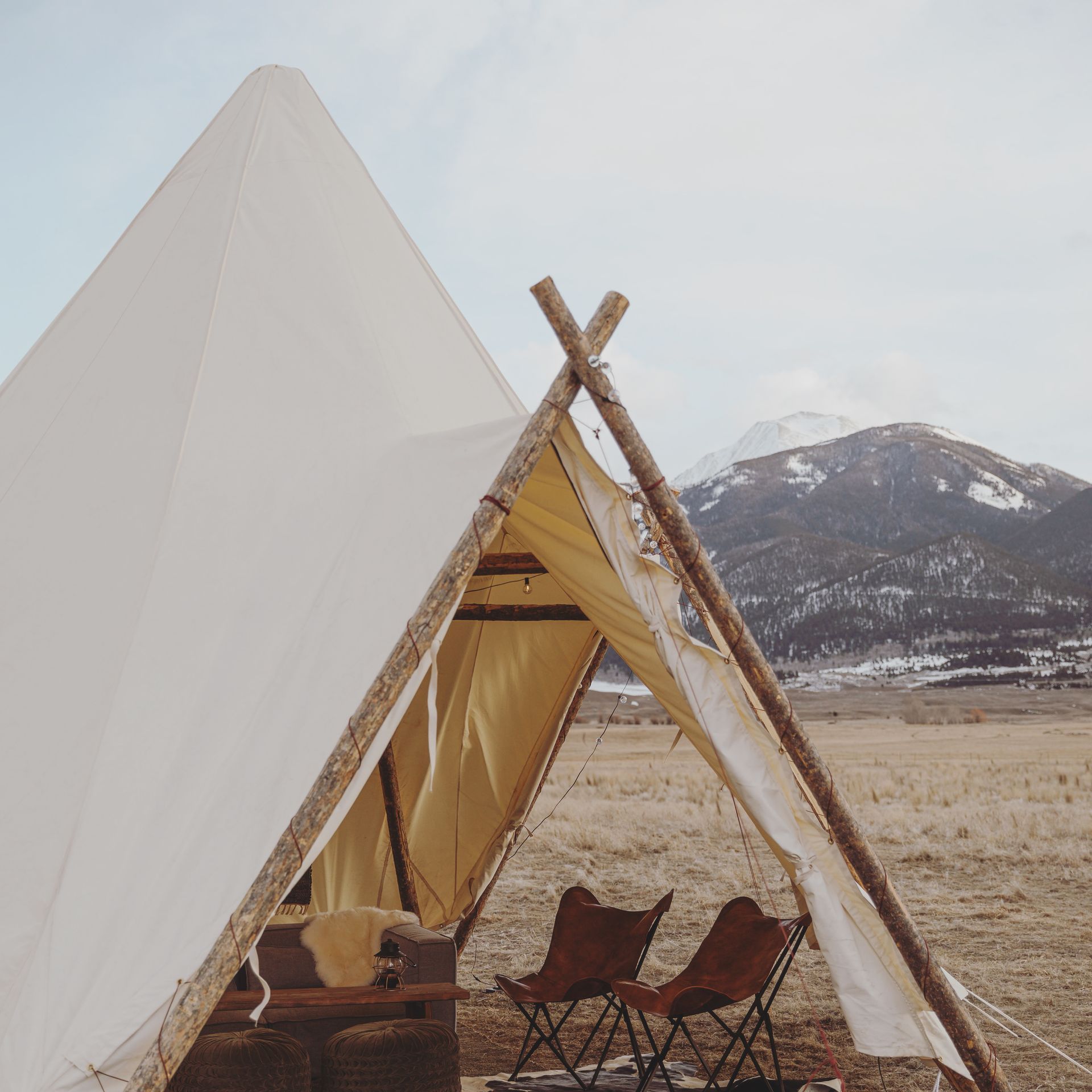 A white canvas tent with wooden frame and two chairs, set in a snowy mountain landscape.
