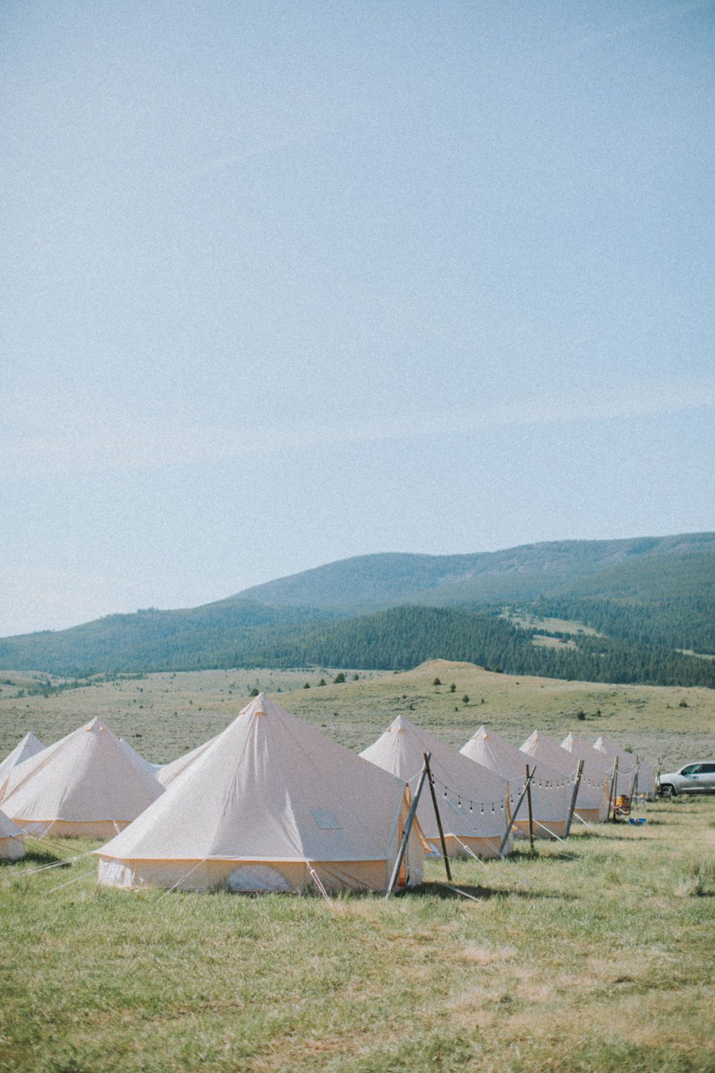 White tents pitched on a grassy field with hills and blue sky in the background