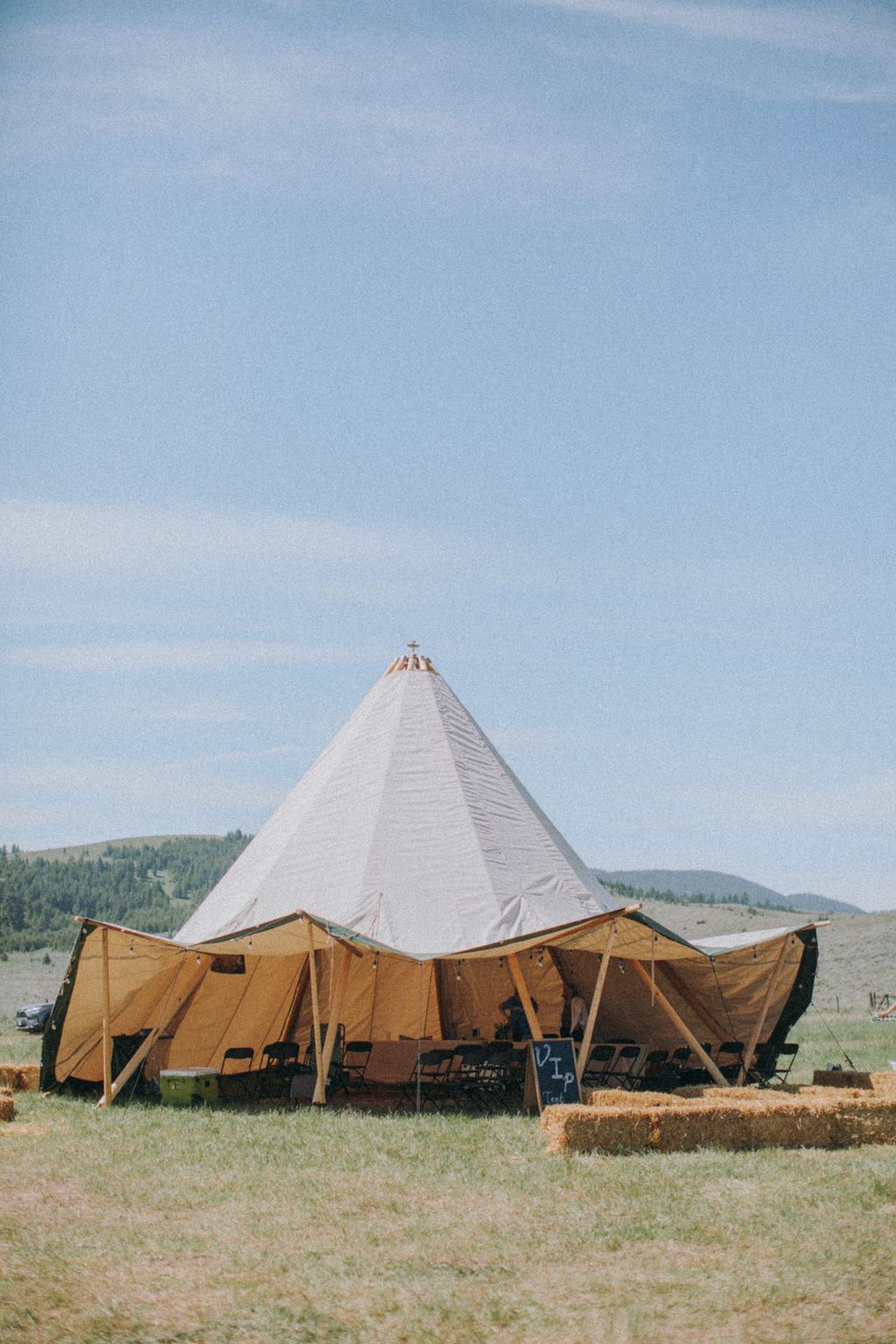 Tan-and-white canvas tent pitched in a grassy field under a clear blue sky