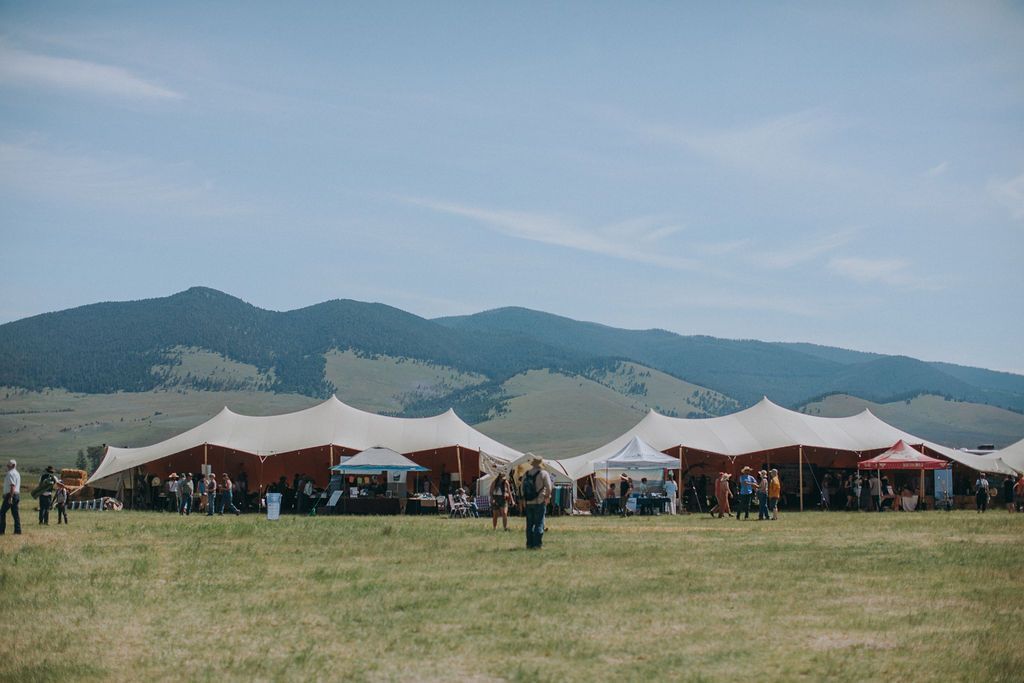 Outdoor festival tents on a grassy field with mountains in the background