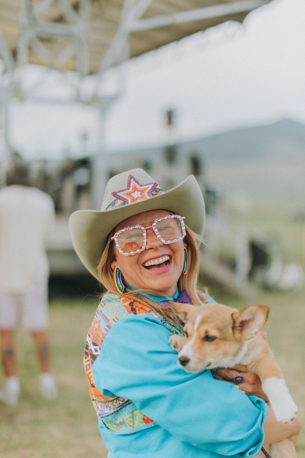 Smiling woman in a cowboy hat holding a small dog outdoors under a white canopy