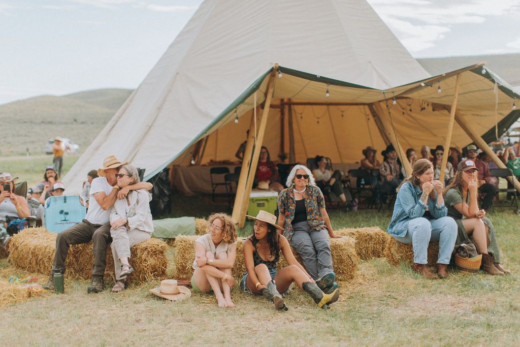 Group sitting on hay bales outside a white tent at a rural outdoor event