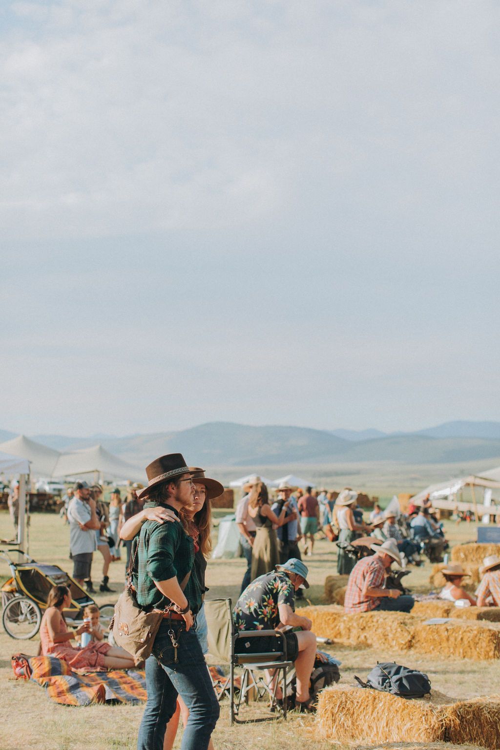 People in a pumpkin patch with hay bales and tents under a cloudy sky