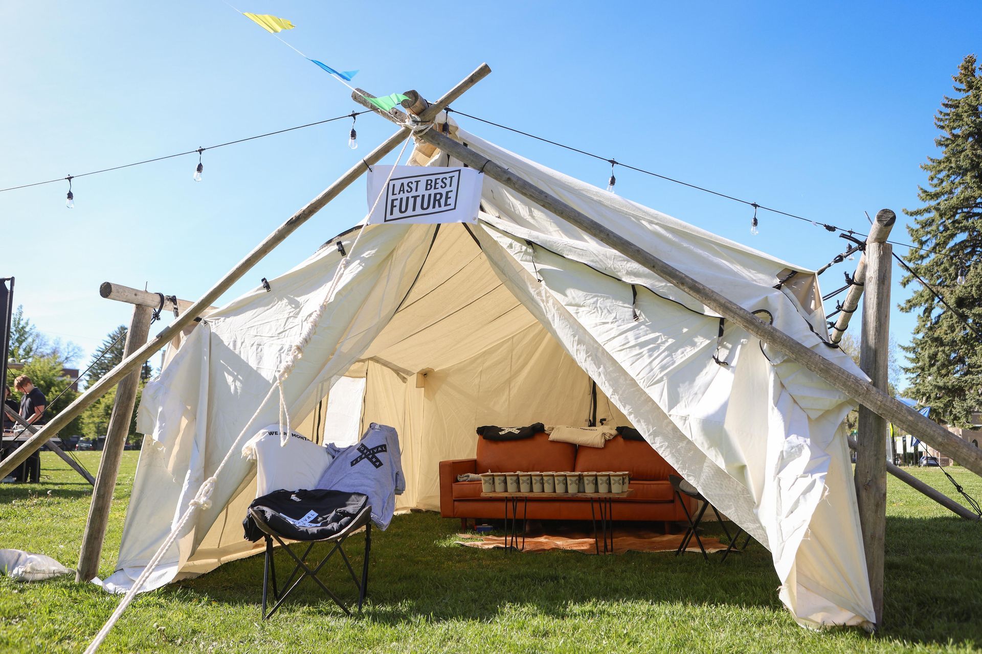 Open white canvas tent on grass with wooden bench inside under a sunny blue sky