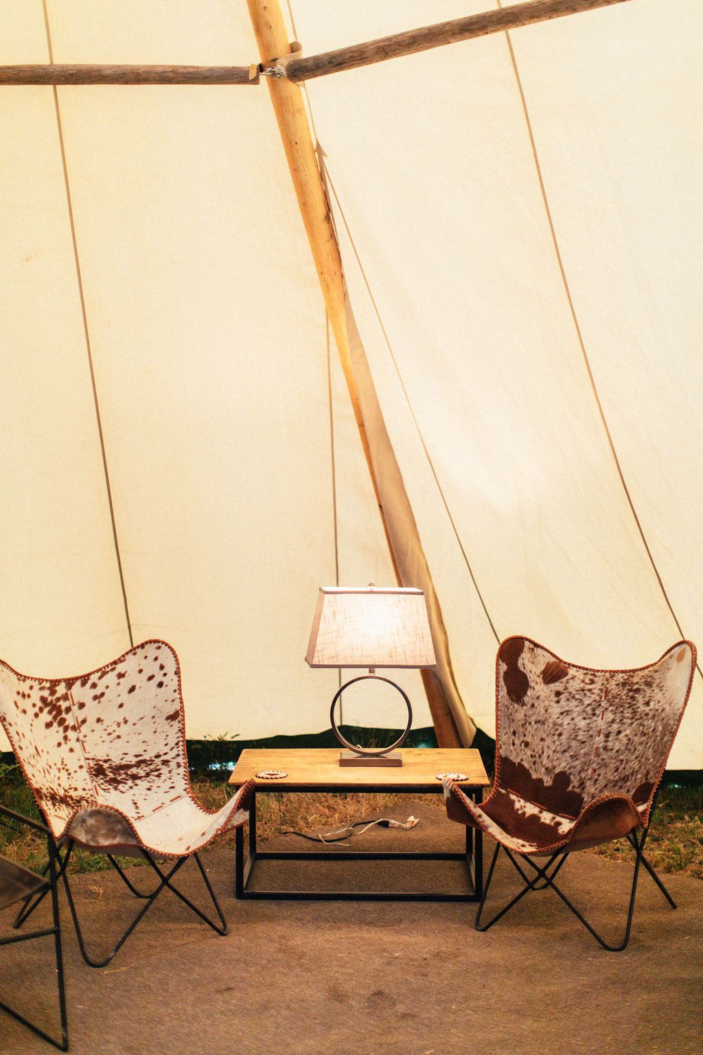 Cozy tent-like room with two patterned chairs, a small table, and a lit lamp against beige fabric walls