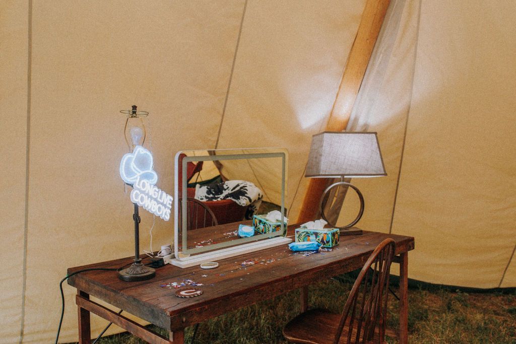 Desk with mirror, lamp, and chair inside a tan tent-like room.