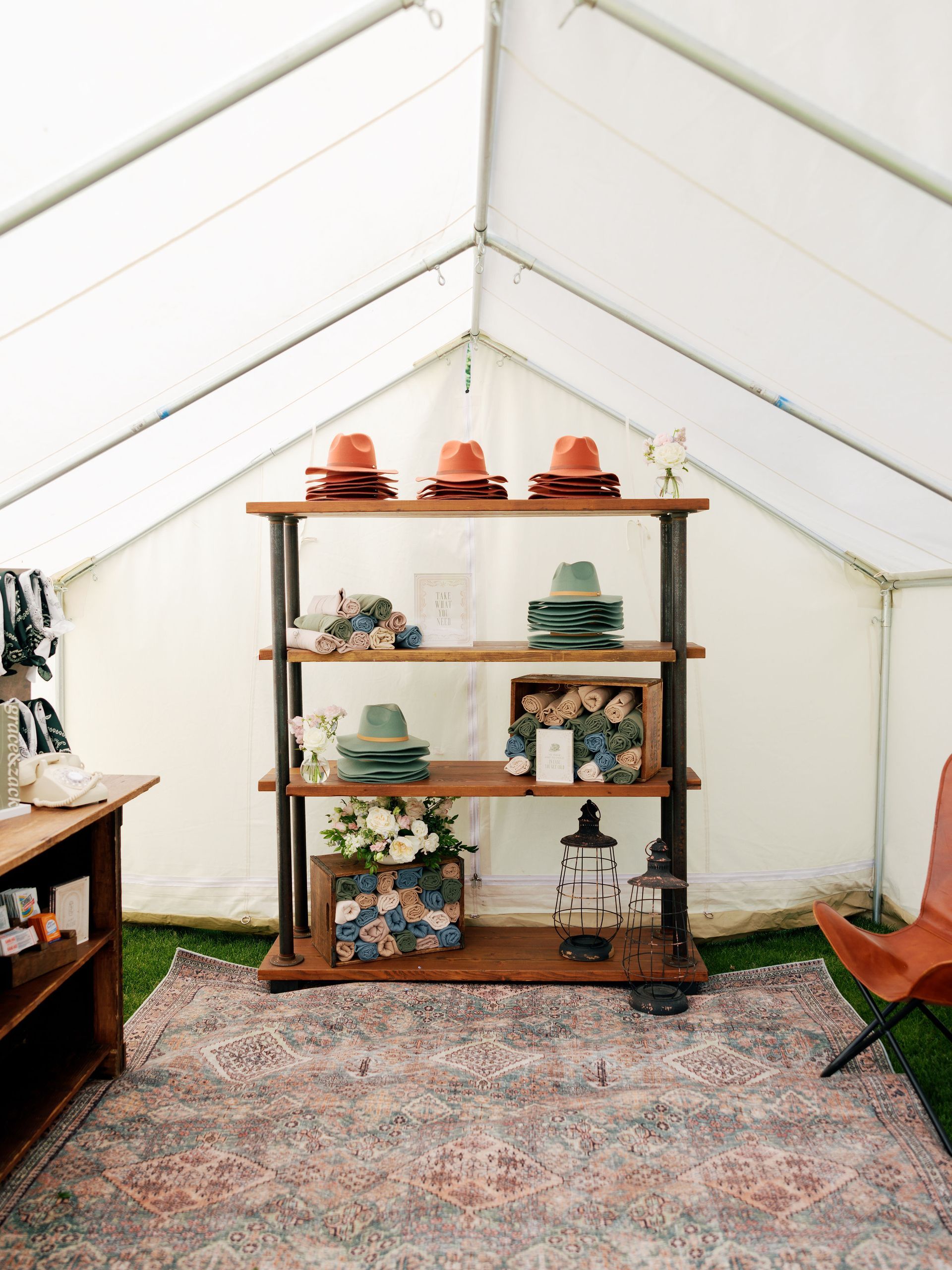Wooden shelf in a white tent displaying pottery and decor on a patterned rug.