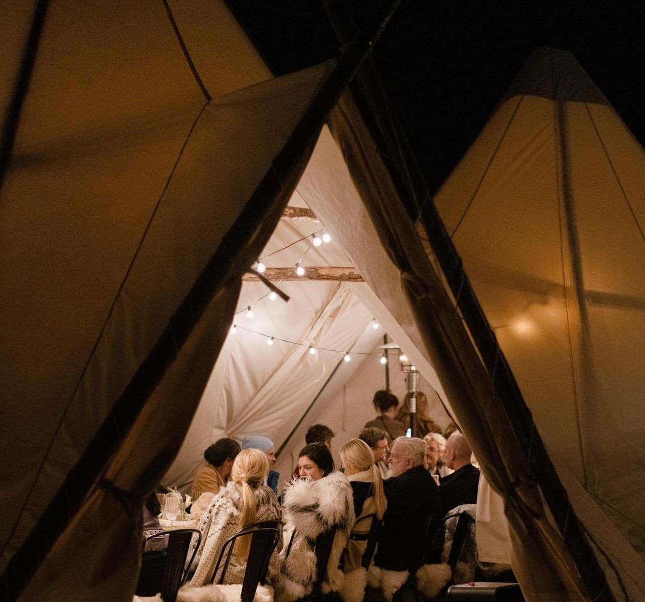 Guests seated inside a warmly lit tented event space at a formal gathering