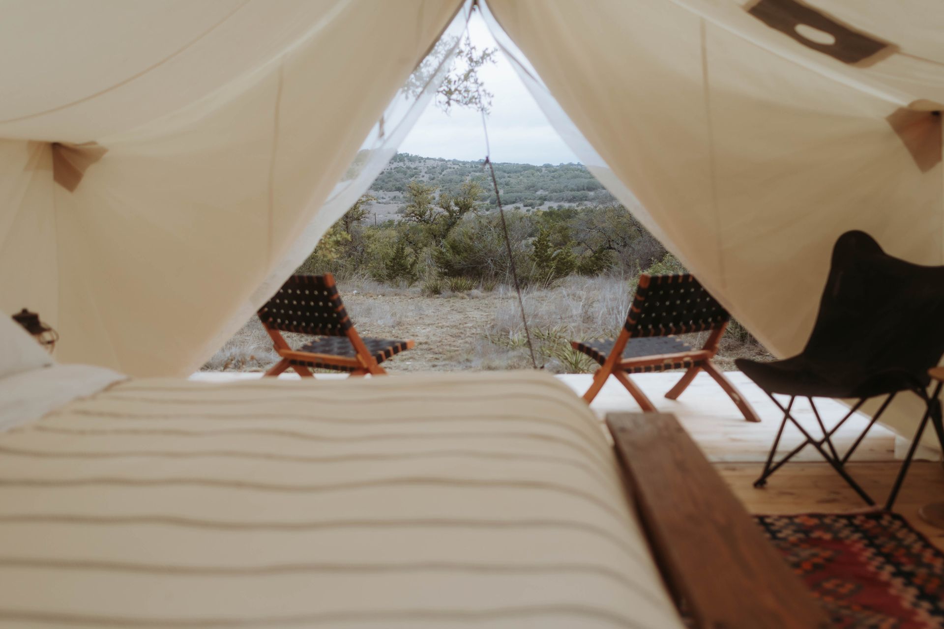 Inside a tent, two wooden chairs face a desert view beyond the open flap.