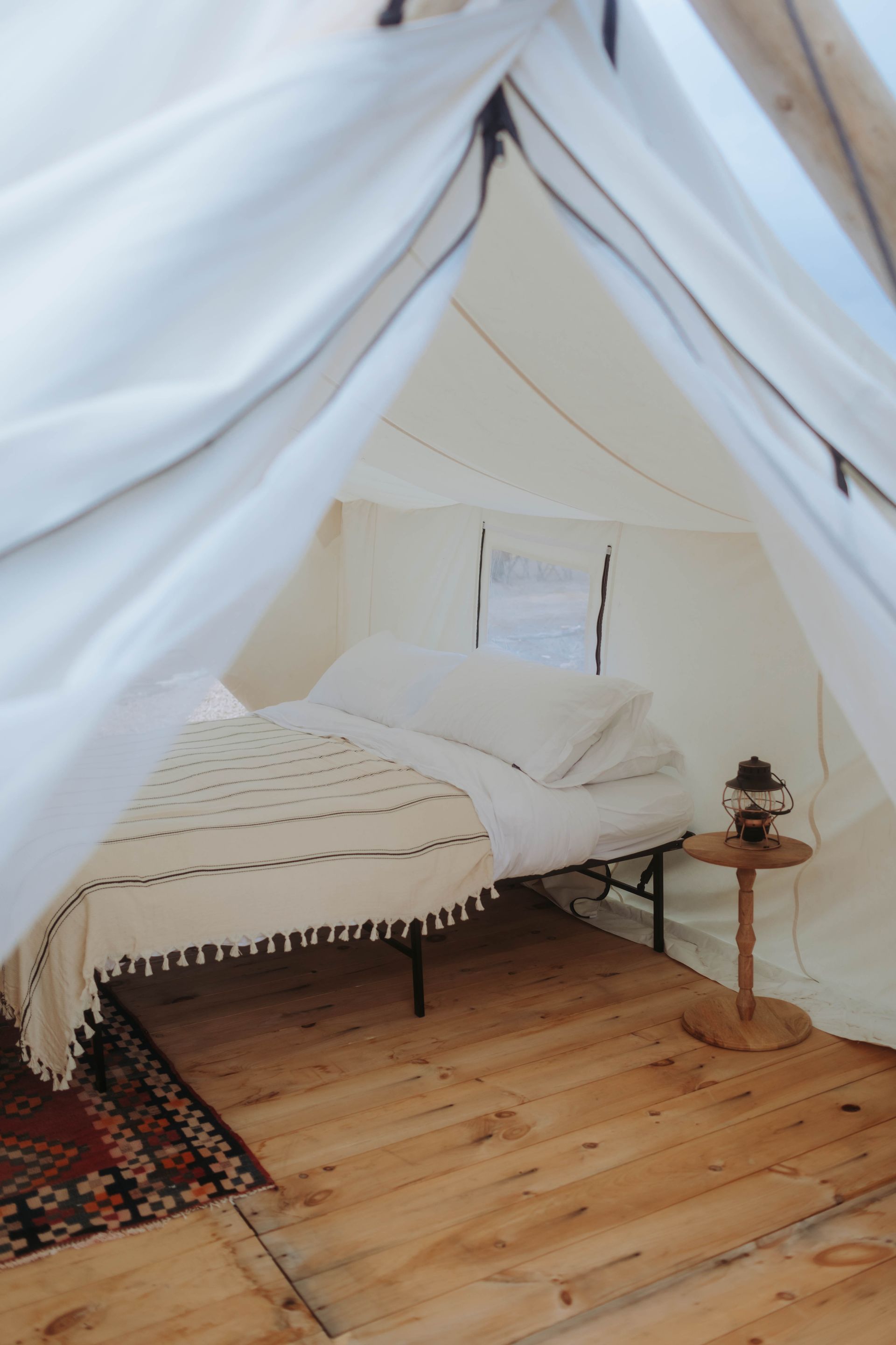 White tent-style bedroom with a bed, wood floor, and small side table with lantern