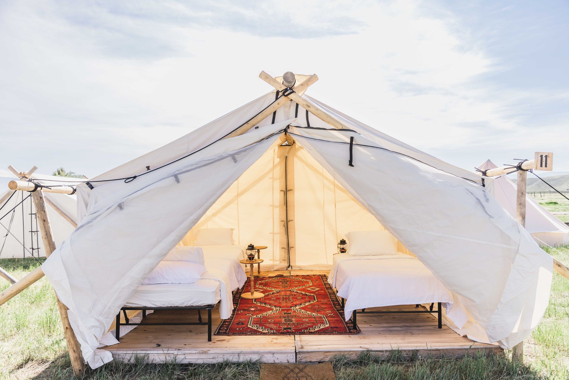 Open-front white tent with two beds and red rug in a grassy field