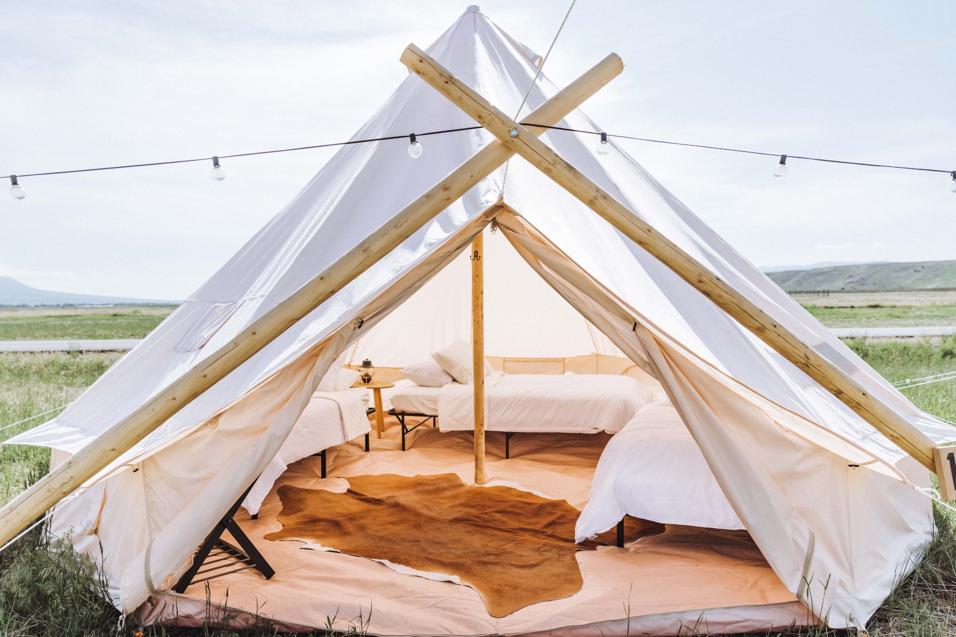 Open white canvas tent with bed and rug in a grassy outdoor field