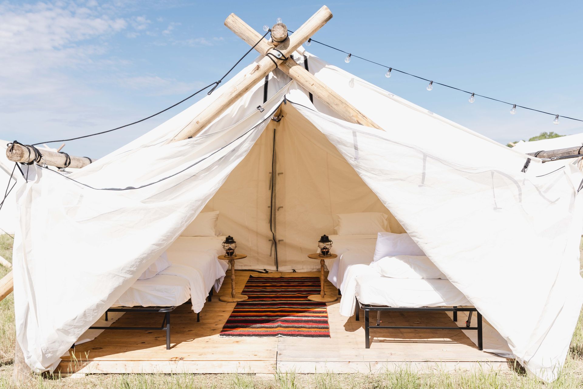White canvas tent interior with two beds and a red patterned rug, viewed from the entrance