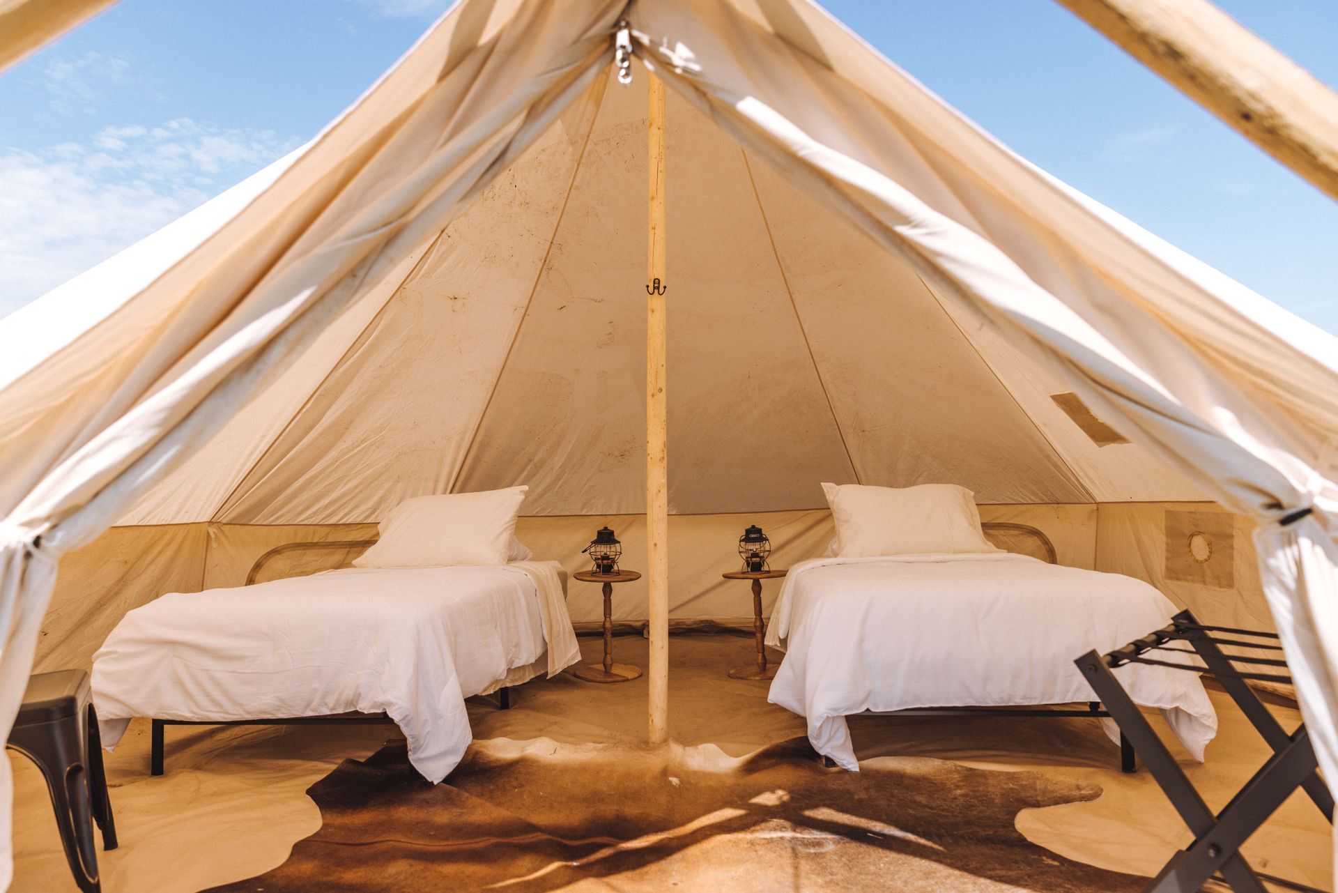 Two white beds in a beige glamping tent with open flaps and a central pole