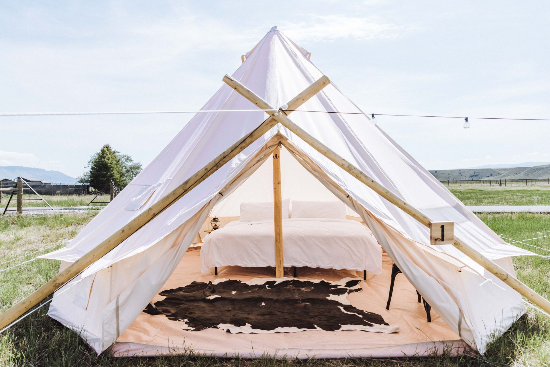 White canvas tent with wooden frame and bed in a grassy field under a bright sky