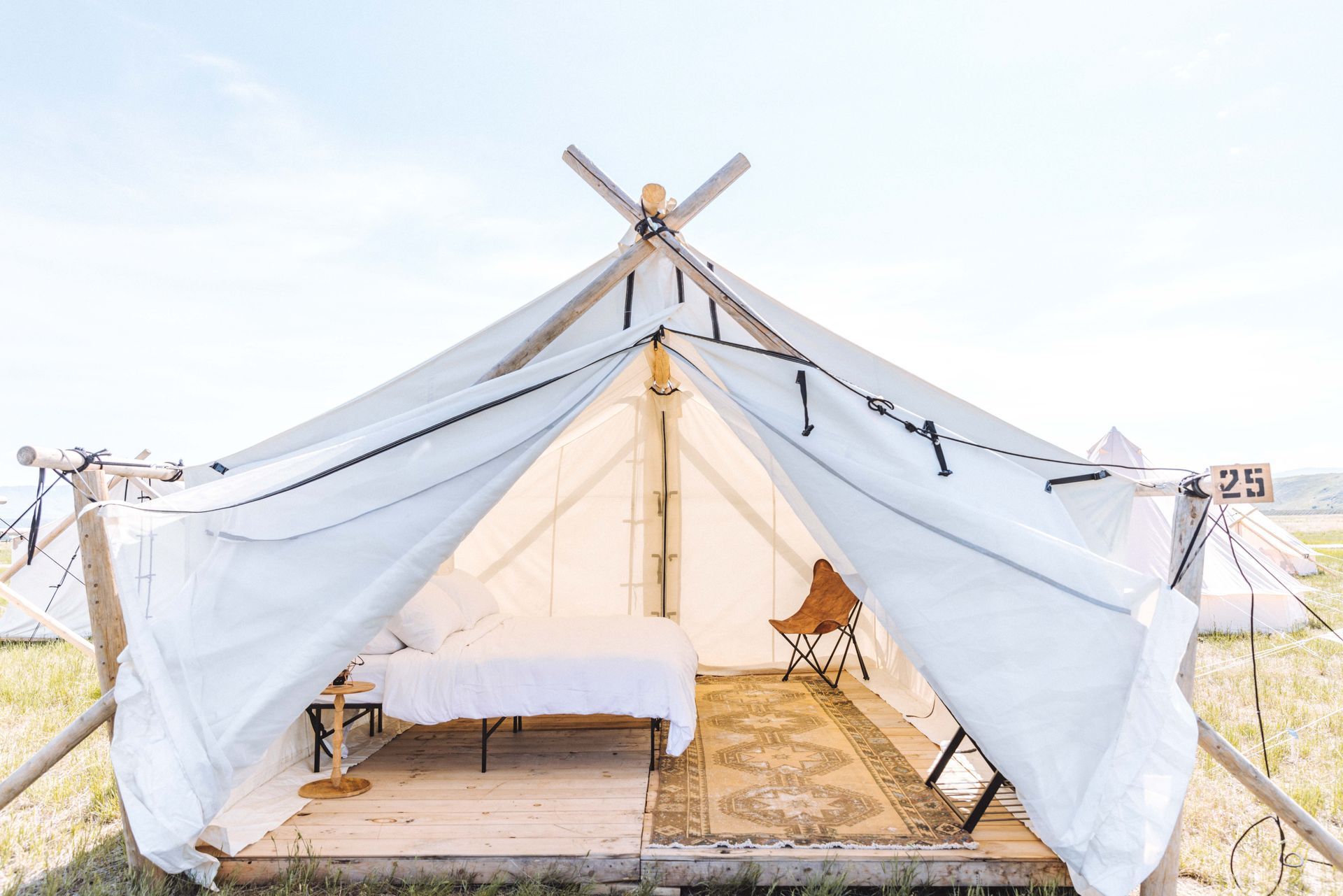 Bright white tented glamping suite with bed and seating on a wooden deck by the beach