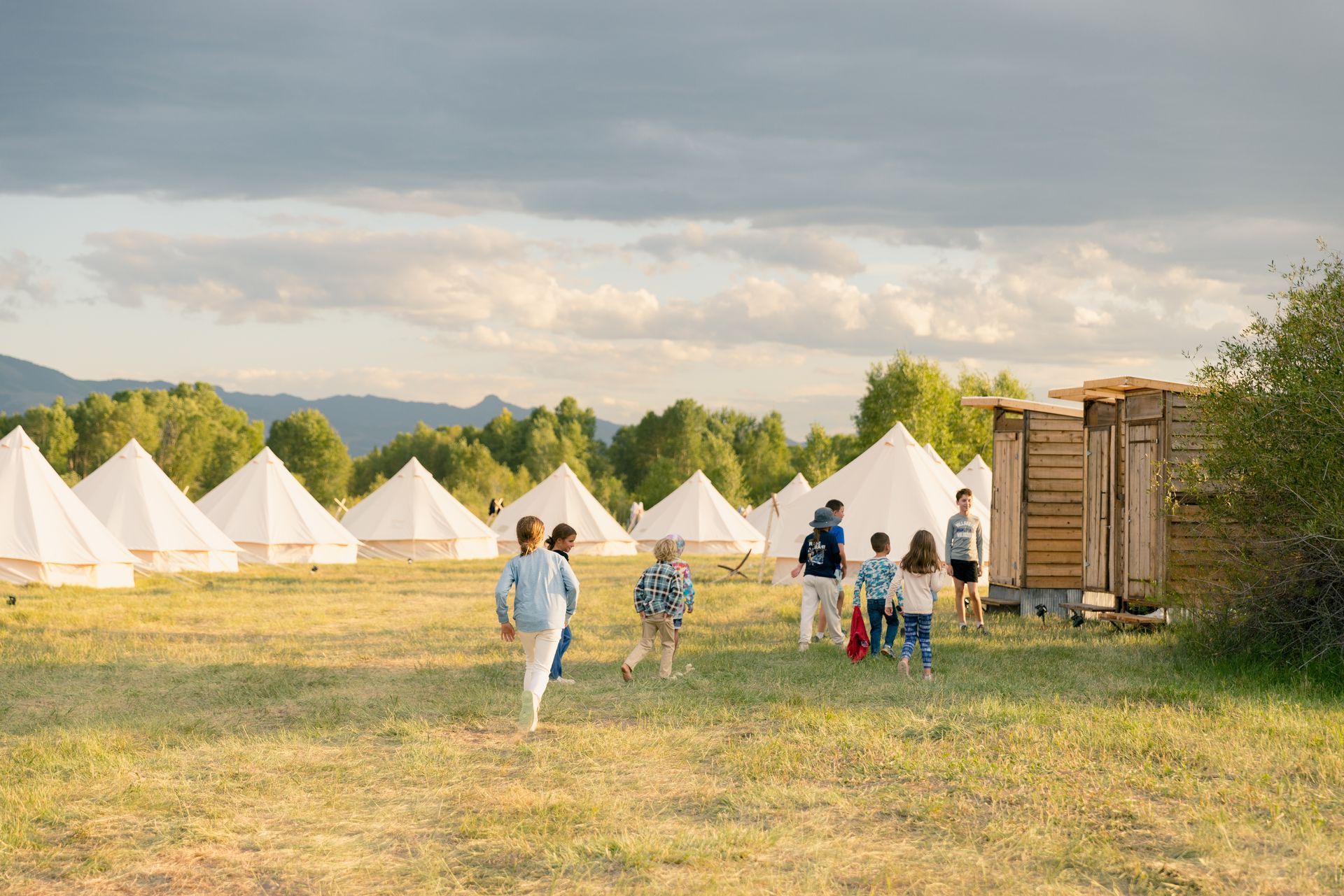 Children walking toward white tents in a grassy campsite at sunset