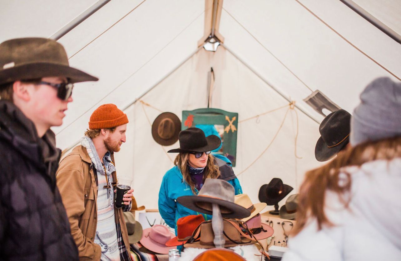 People gathered inside a white tent, playing music around a drum and guitars.