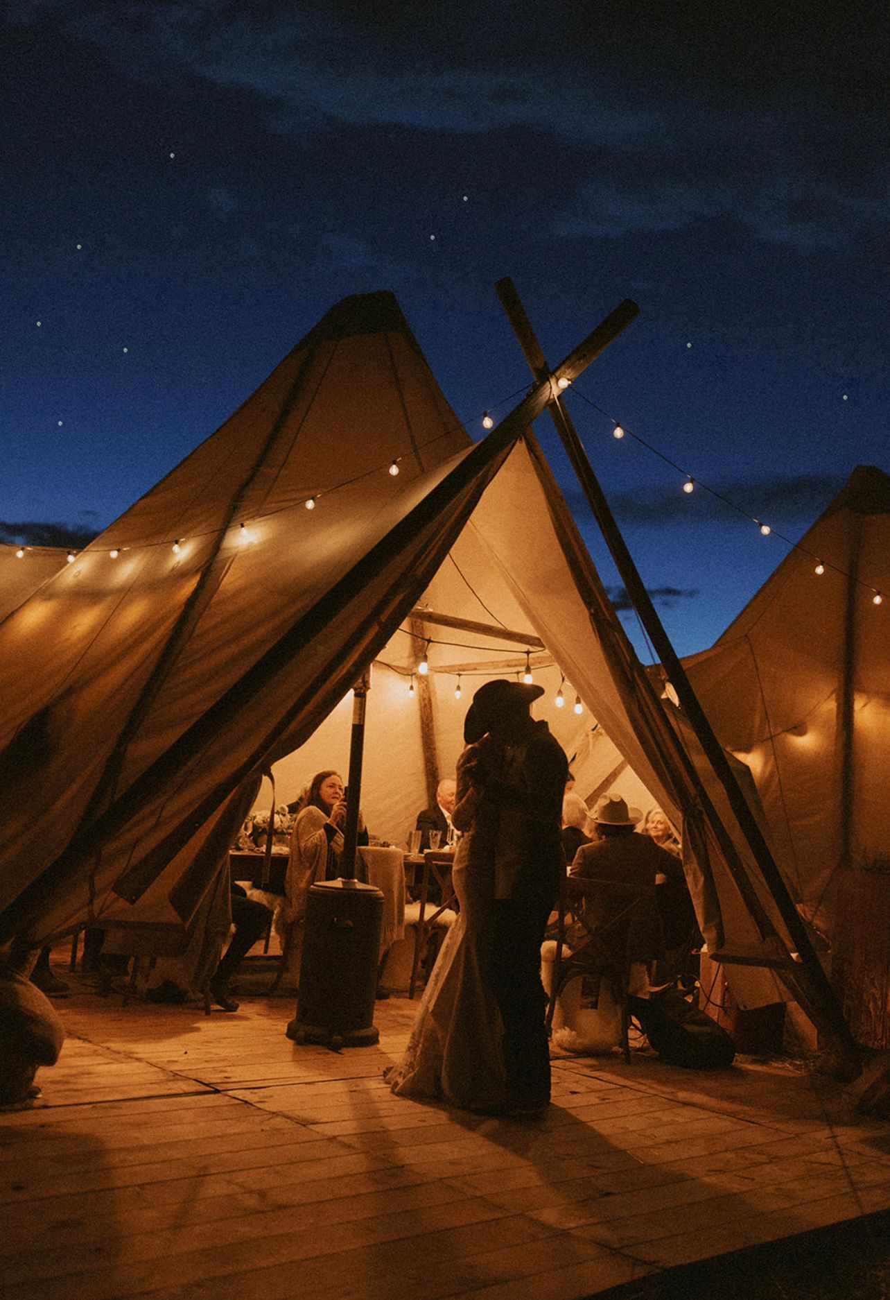 Lit candlelit desert tents under a starry night sky, with people gathered inside and around them.