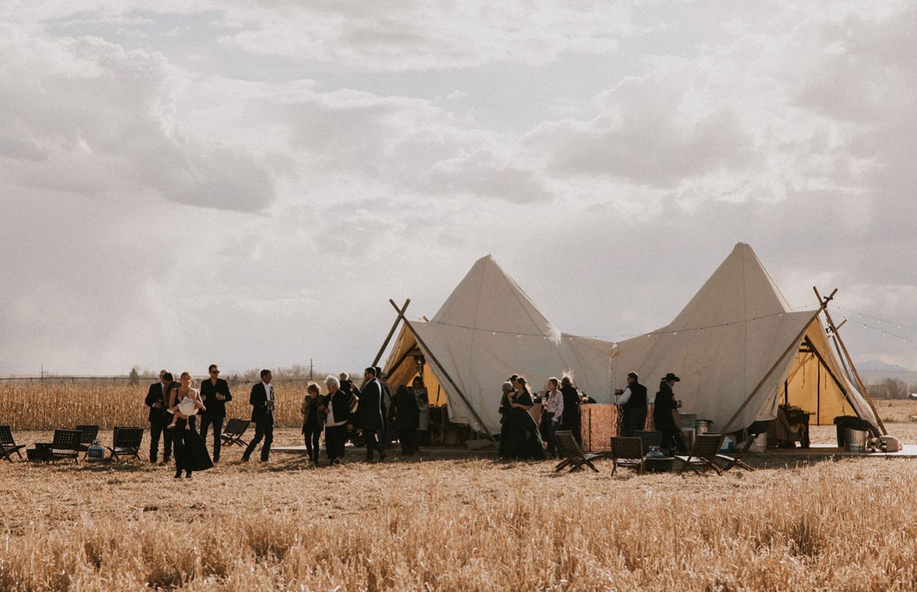 Tents and people gathered in a dry field under a cloudy sky, with mountains in the distance.