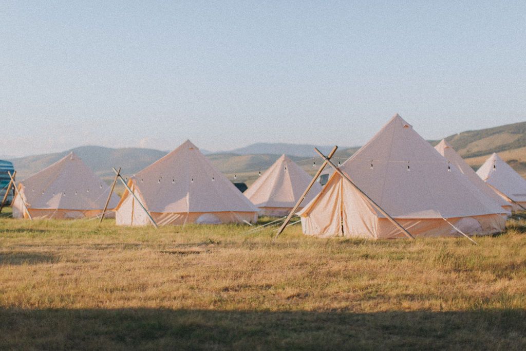 White tents on a grassy field with mountains in the background at sunset