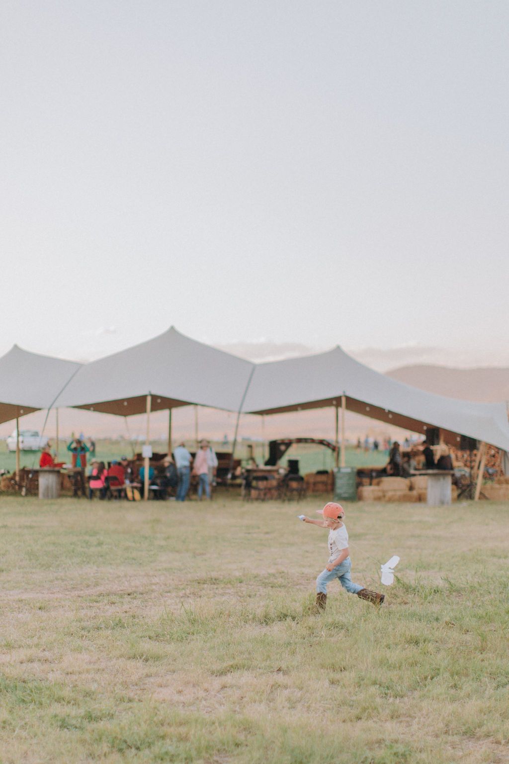 Child running across grassy field near tents and seated people under a hazy sky