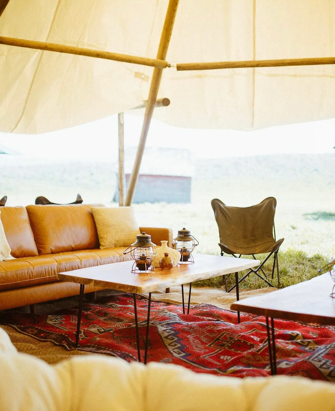 Stylish tent lounge with sofa, coffee table, chair, and red patterned rug overlooking a bright landscape