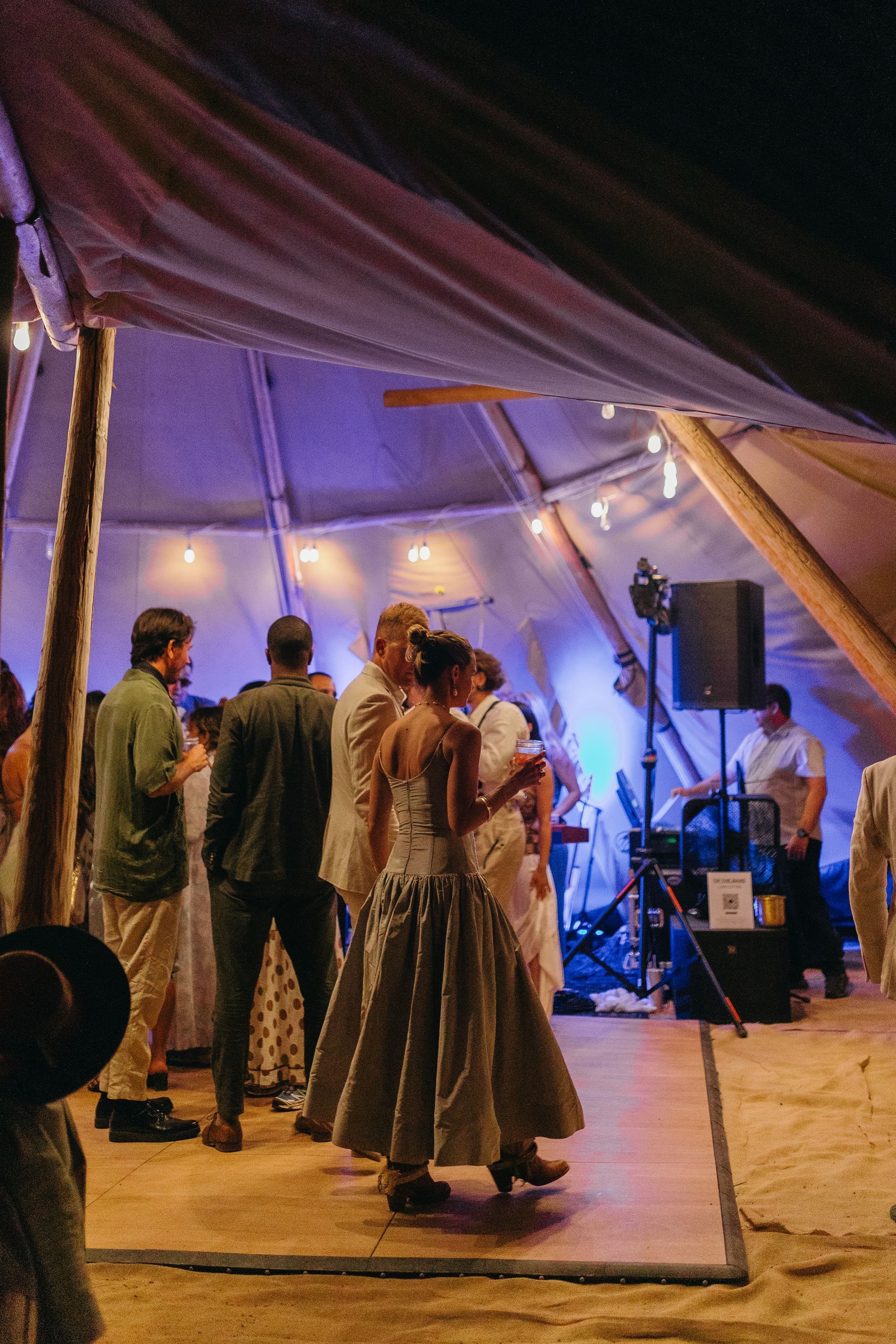 People dancing under a lit tent at night, with musicians and speakers in the background.