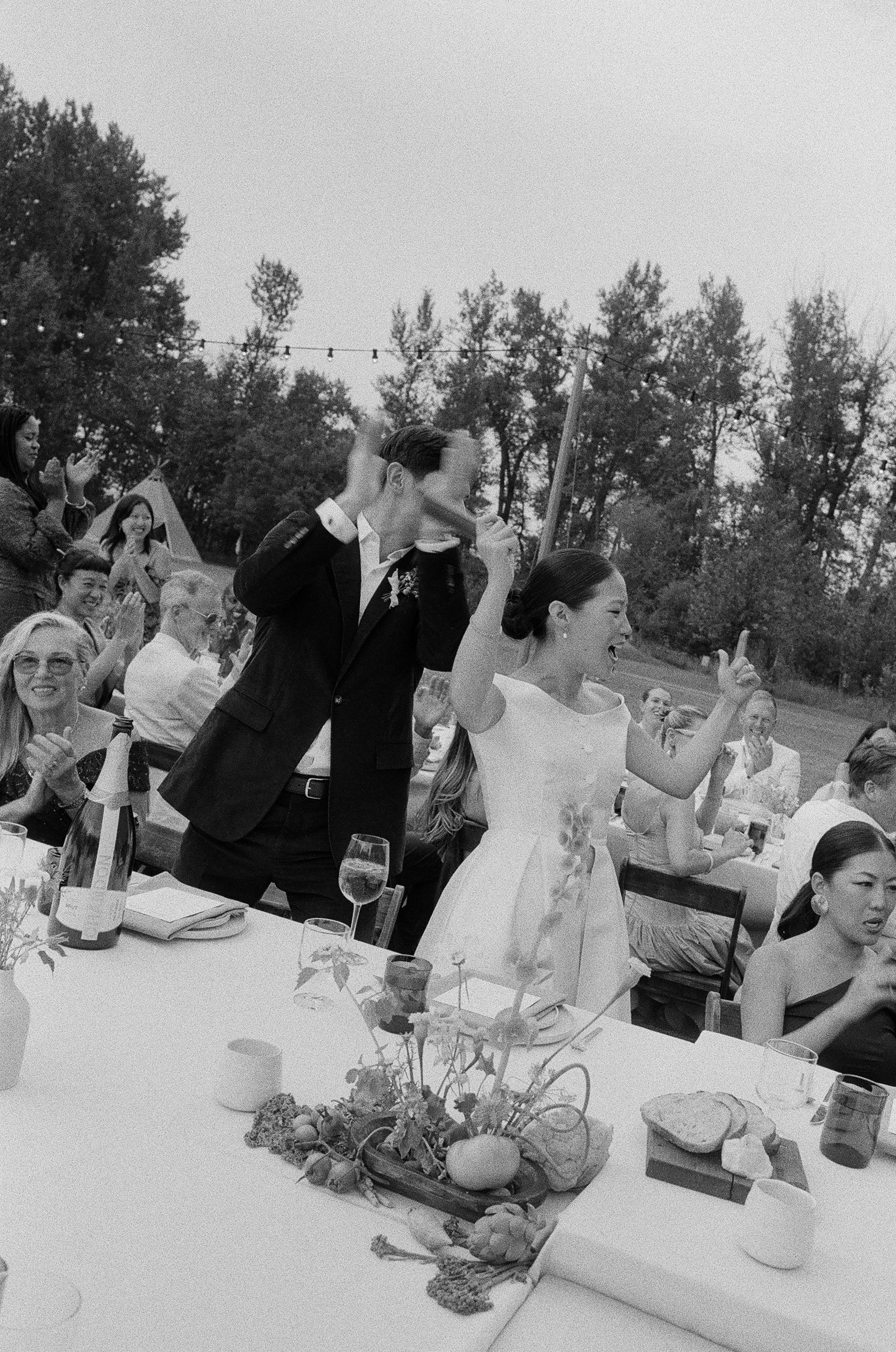 Outdoor wedding reception with guests raising glasses at a decorated table