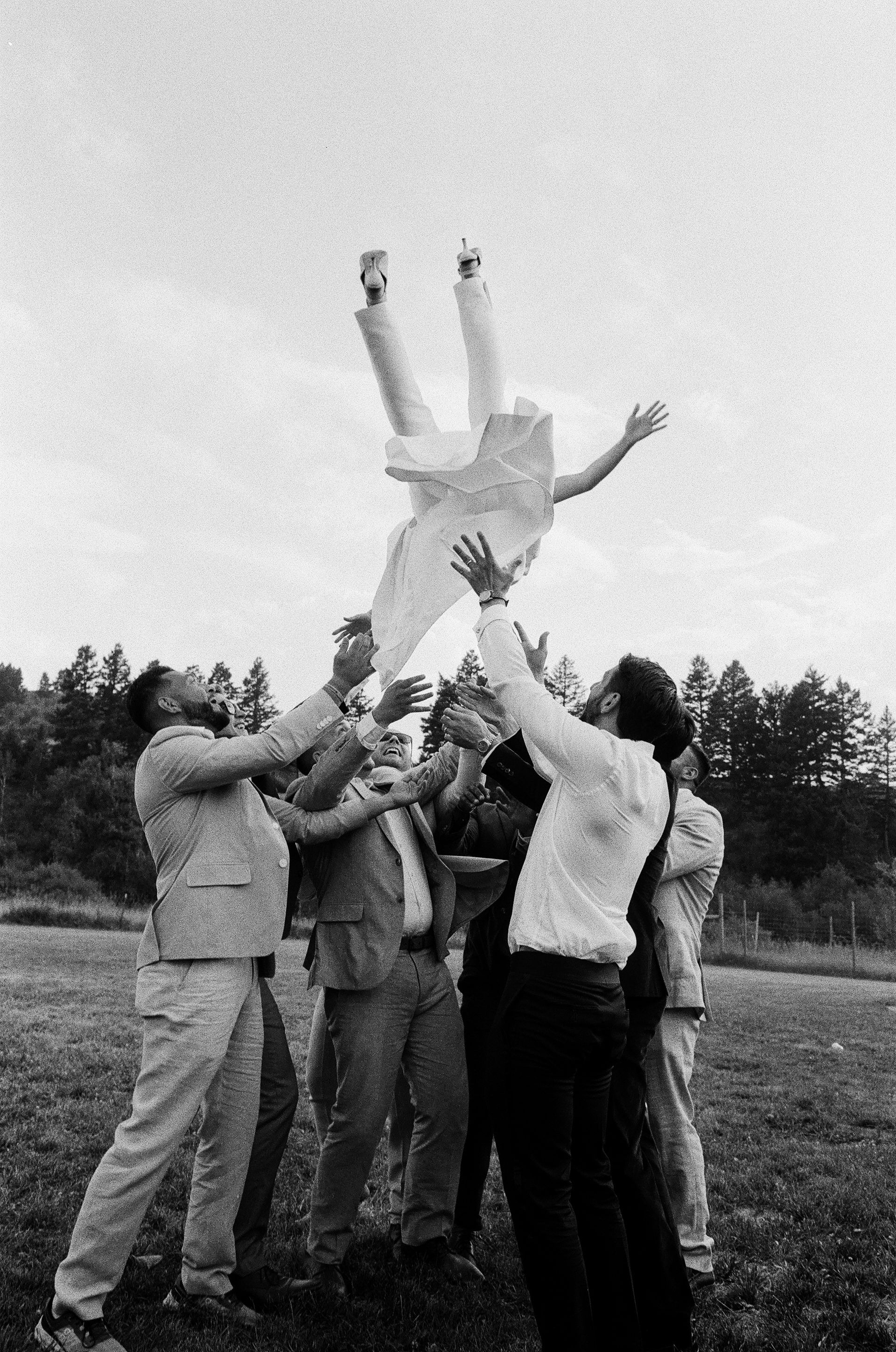 Group of people tossing another person into the air outdoors in a field, black-and-white photo