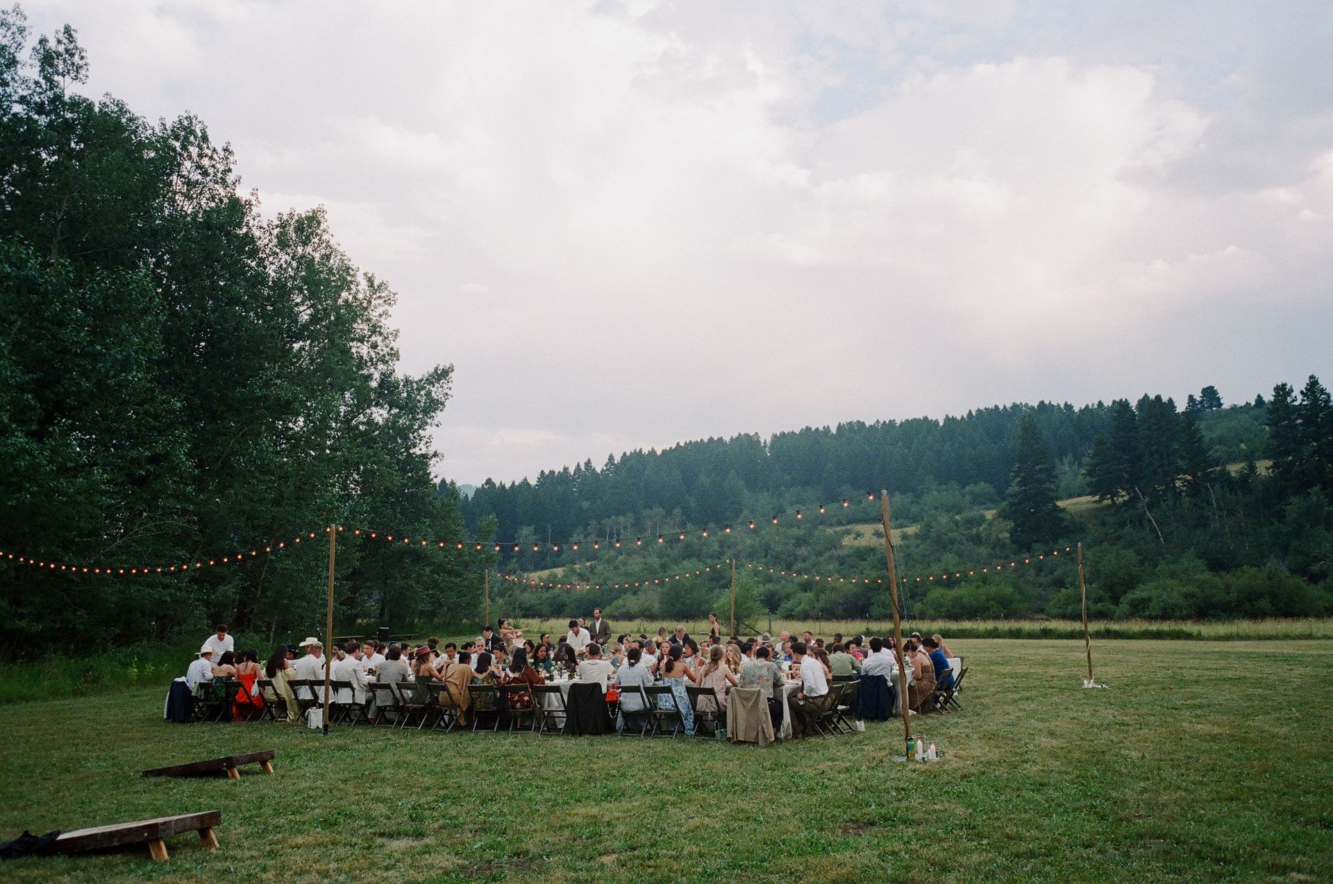 Crowd gathered outdoors on a grassy field near trees and hills under an overcast sky