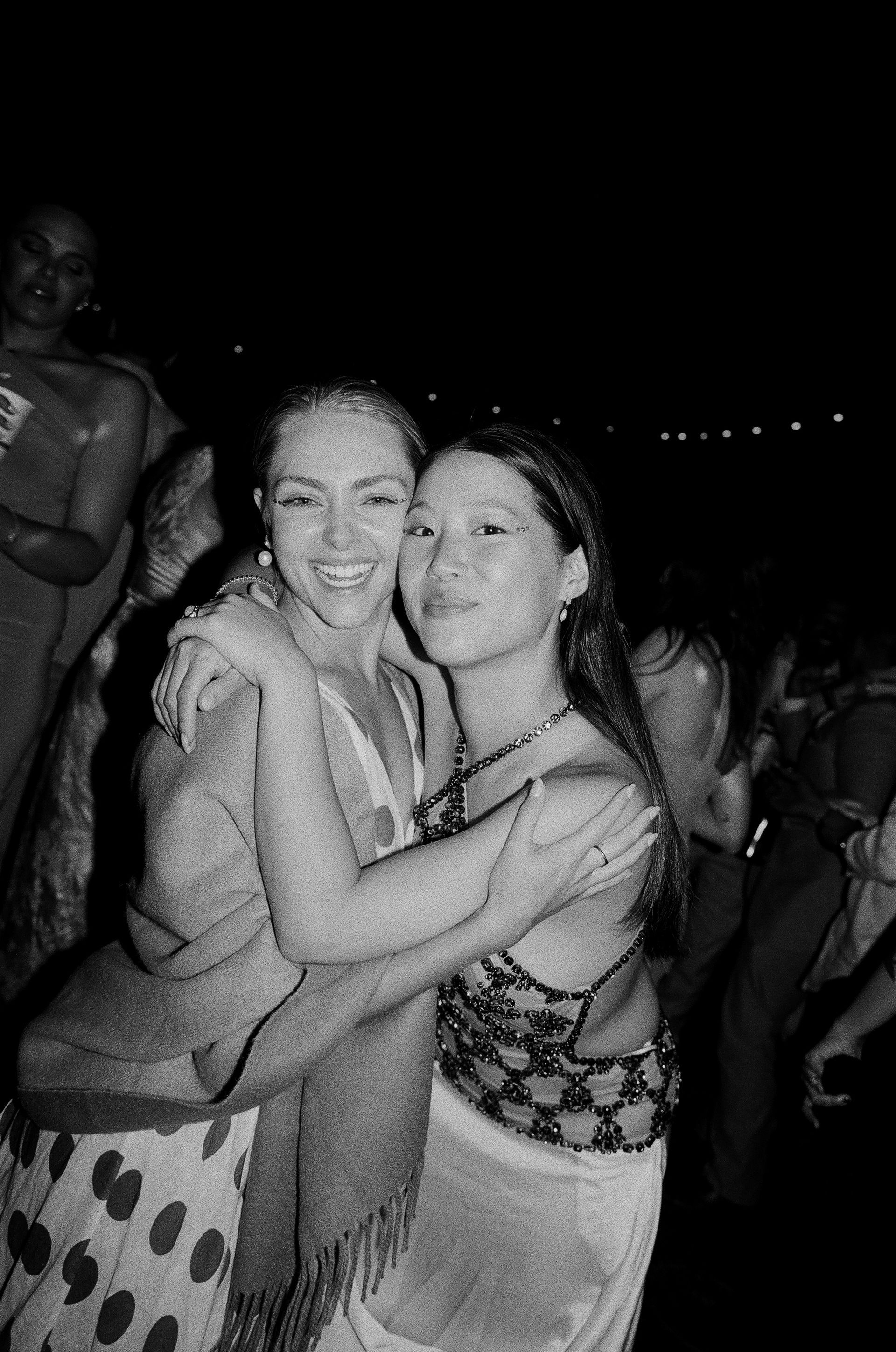 Two people hugging and smiling in a dimly lit crowd at night.