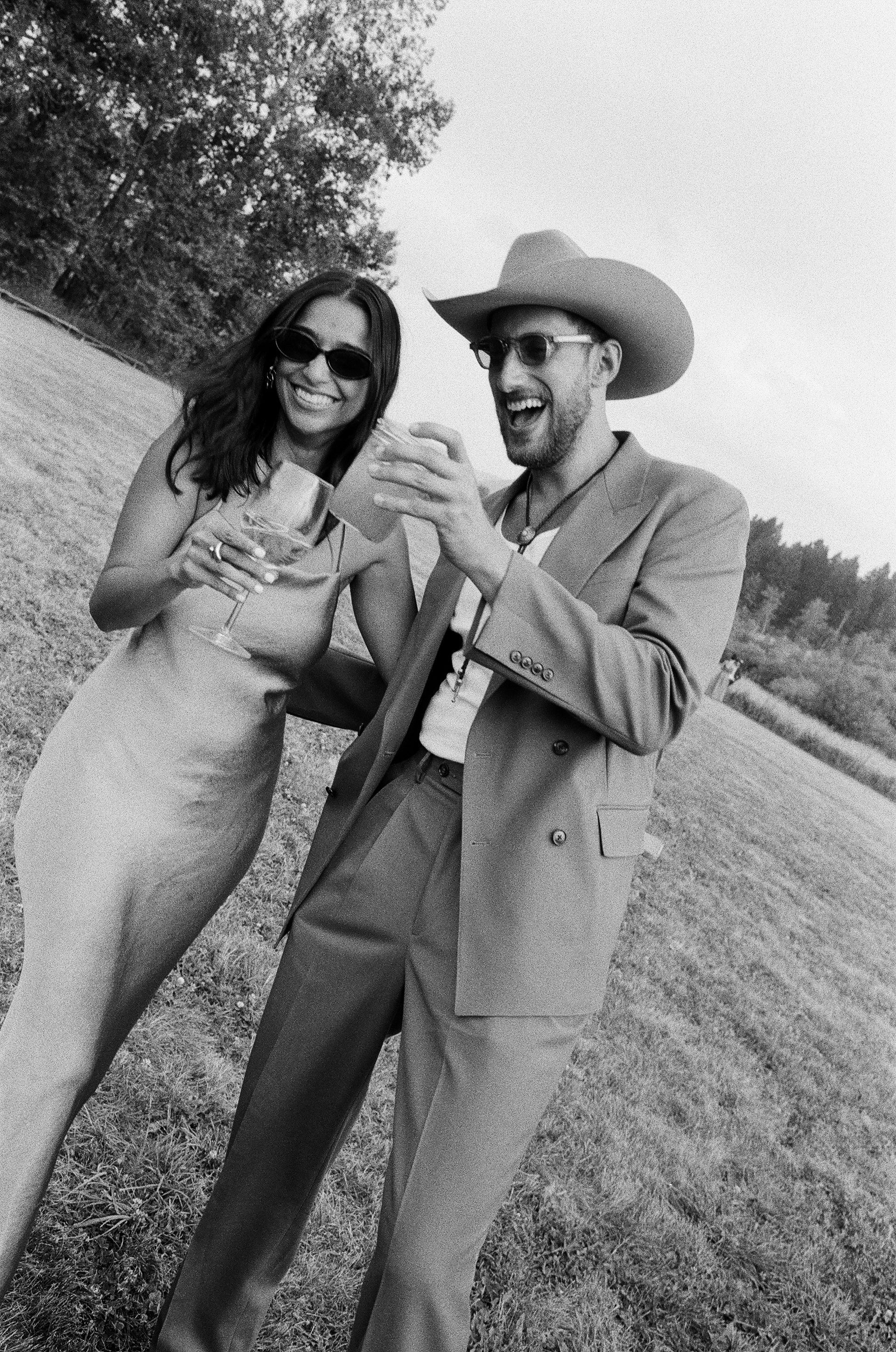 Two people smiling and posing outdoors on a grassy path, one wearing a cowboy hat.
