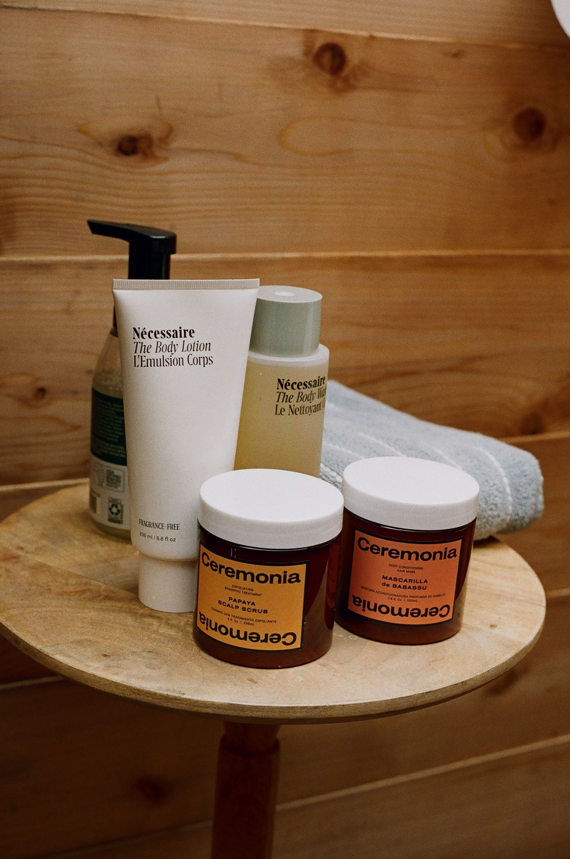 Assorted lotion and cream jars on a wooden shelf, with a pump bottle and towel in the background
