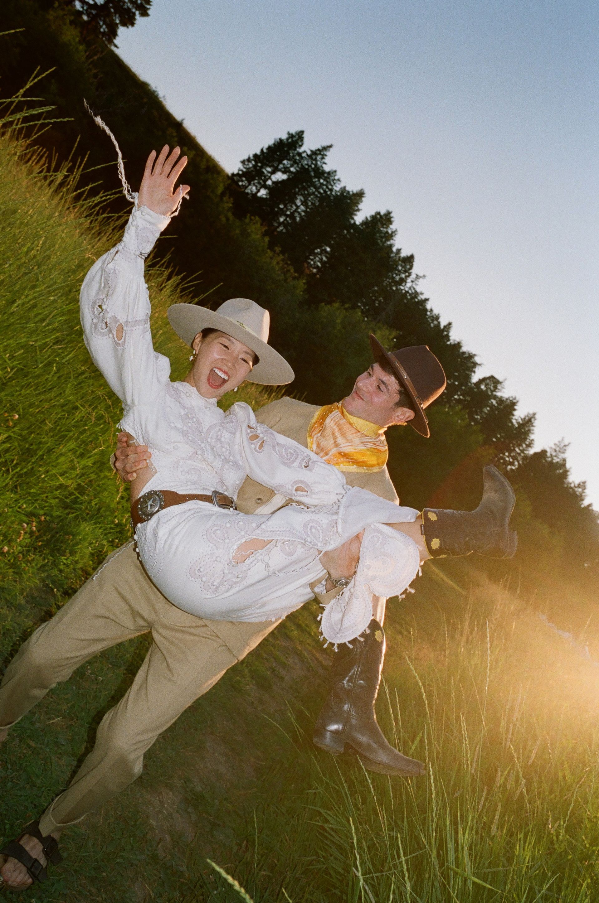 Three people in hats posing in a grassy field at sunset
