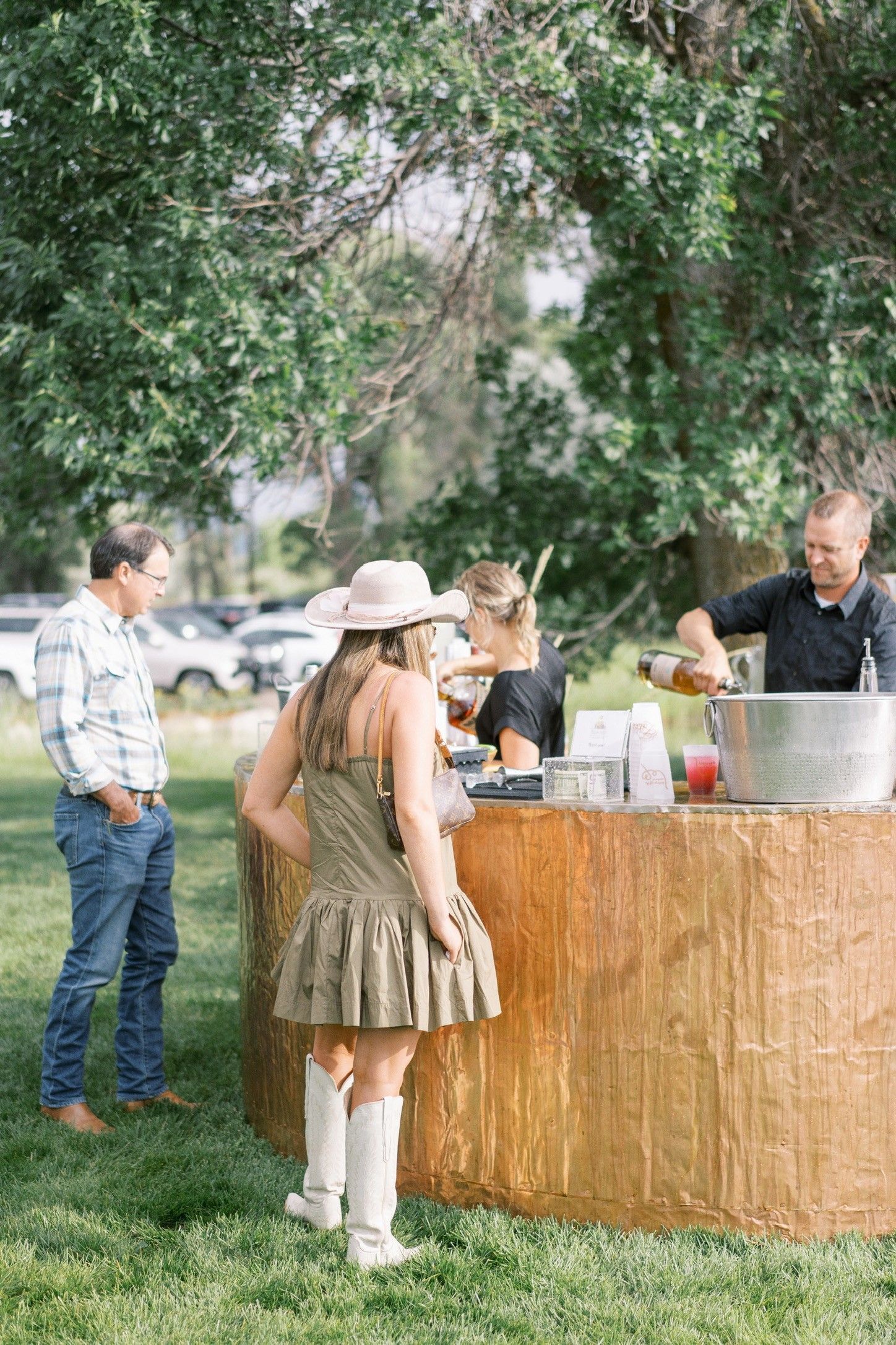 People gathered around an outdoor drink station at a park, with trees and grass in the background.
