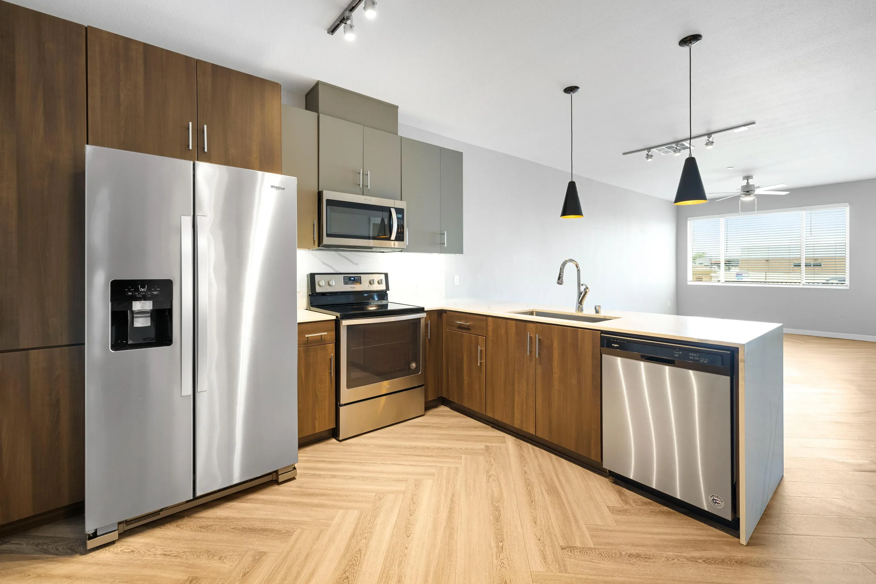 Open-concept kitchen with stainless steel fridge, oven, microwave, dishwasher, and wood cabinets.