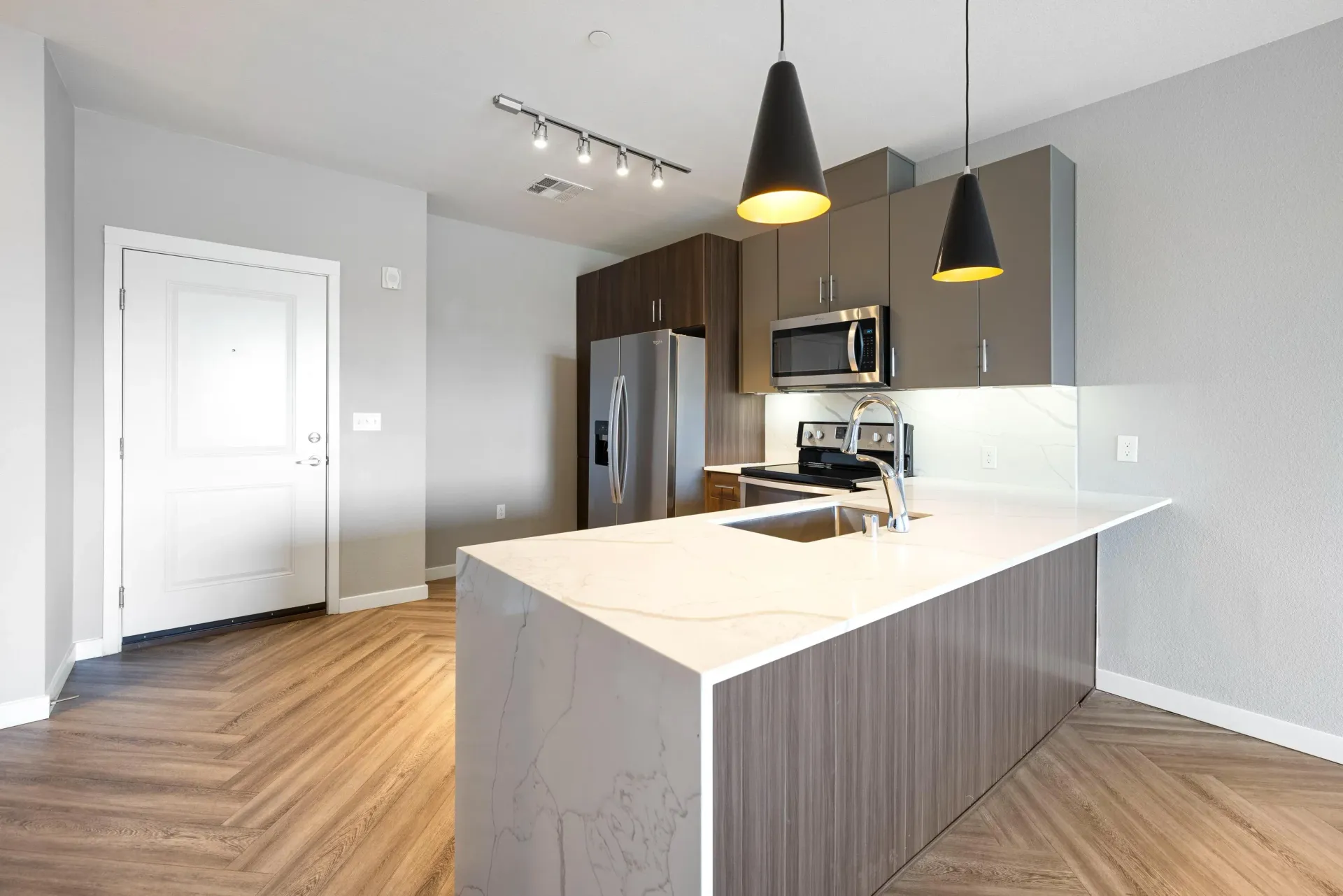 Interior view of a modern apartment kitchen with an island, stainless-steel appliances, and pendant lights at Olympus Alameda, offering apartments in Albuquerque, NM.