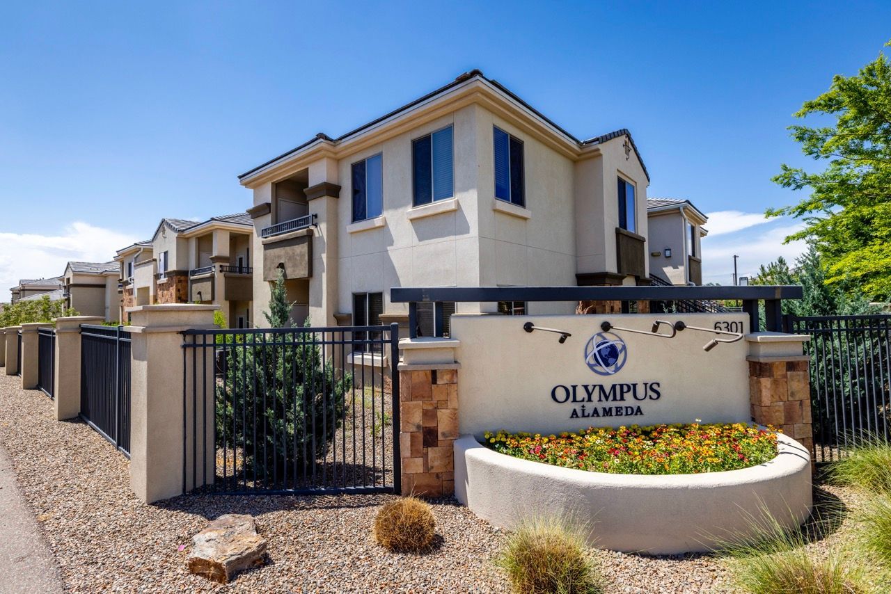 Gated entry to Olympus Alameda apartment community with beige buildings and a landscaped sign at Olympus Alameda, offering pet-friendly apartments in Albuquerque.