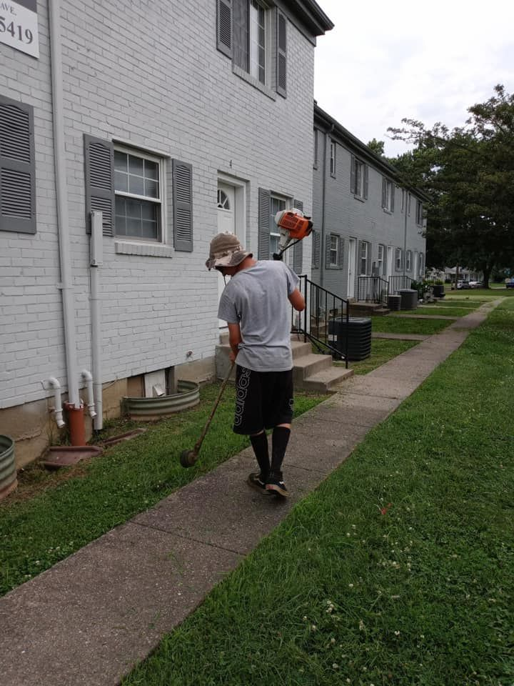 A man is mowing the grass on the sidewalk in front of a building