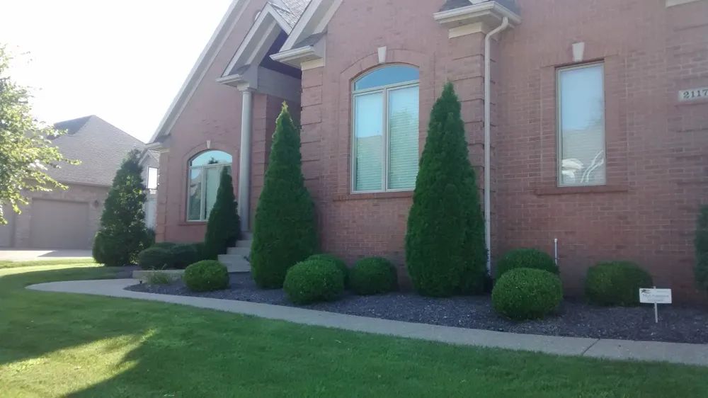 A brick house with a lush green lawn and trees in front of it.