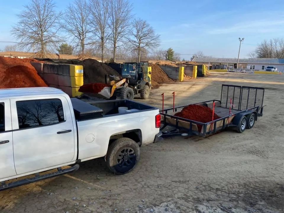 A white truck is pulling a trailer full of dirt.
