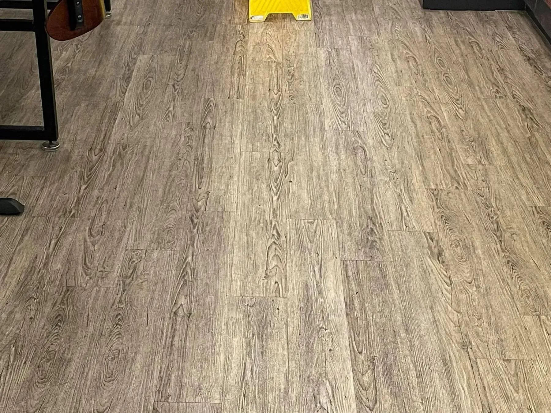 Wood-look flooring in a room, with chair legs at the left and a yellow object near the top center.