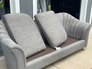 Gray sofa with two back cushions, in front of a window.