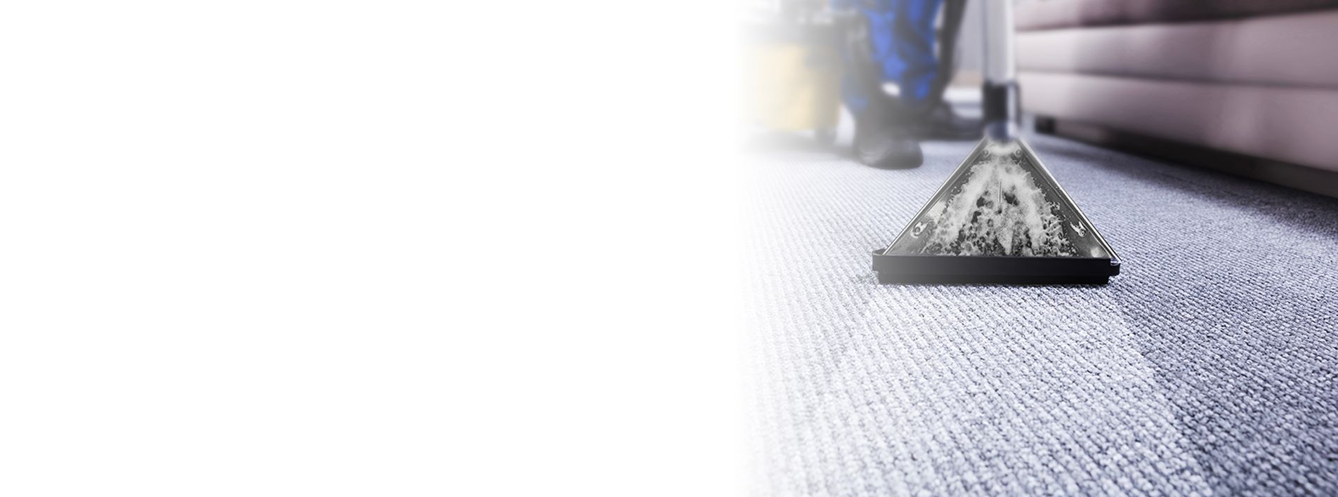 Carpet being cleaned with a machine; part of a leg and couch visible.