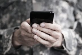 Hands holding a black smartphone against a blurred outdoor background.